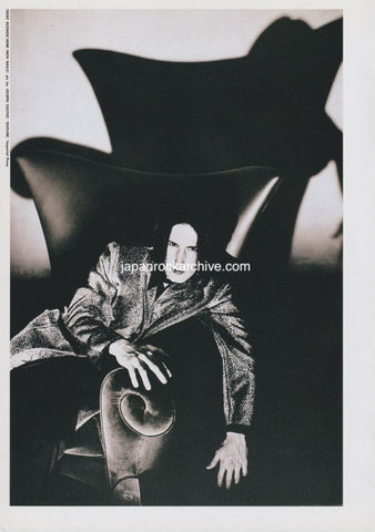 Black and white photograph of trent reznor of nine inch nails in a dramatic pose sitting in a huge chair
