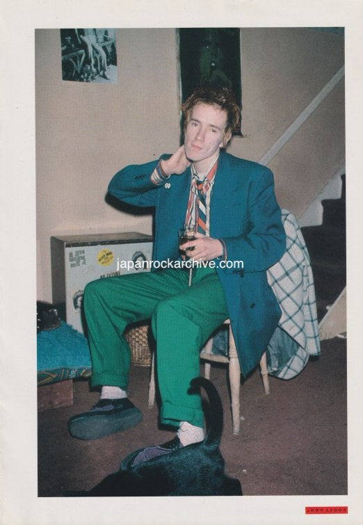 John Lydon of PIL sitting on a chair with a drink in hand, wearing a green suit and tie, from a Japanese music press cutting.
