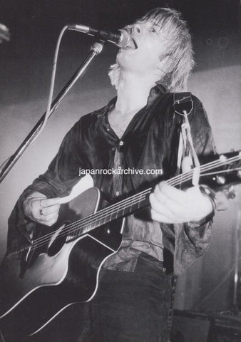 Thom Yorke of Radiohead playing guitar and singing into a microphone on stage.
