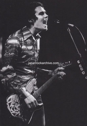 Billy Corgan of Smashing Pumpkins on stage playing guitar and singing into a microphone.